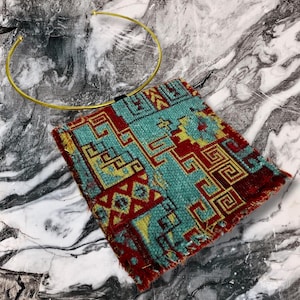 May include: A gold metal choker necklace with a colorful patterned fabric hanging from it. The fabric has a geometric design with red, blue, yellow, and green colors.