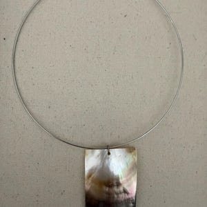 May include: A silver-toned metal wire choker necklace featuring a single rectangular pendant made of iridescent mother-of-pearl. The pendant displays natural swirling patterns of white, cream, and dark brown tones with a smooth, polished finish.