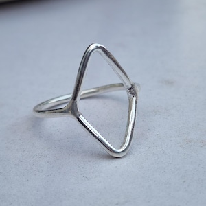 Puede incluir: Un anillo de plata con un diseño geométrico de triángulo abierto. El anillo tiene una banda delgada que conduce a una forma de triángulo abierto más grande. El anillo está hecho de metal plateado brillante.