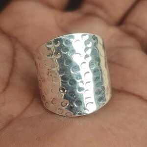 May include: A silver hammered ring with a wide band. The ring has a textured surface and a rounded shape.