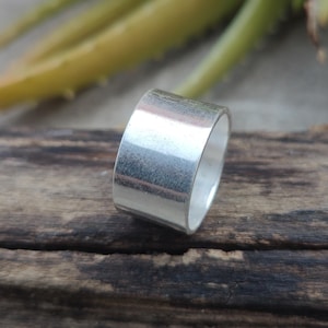 May include: A wide silver band ring with a smooth, polished finish.