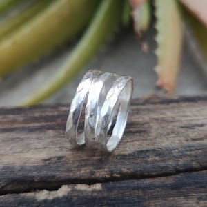 Könnte beinhalten: Ein silberner Ring mit gehämmerter Textur. Der Ring besteht aus zwei ineinander verschlungenen Bändern.