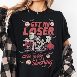 May include: Black t-shirt with a Halloween graphic. The design features three horror movie characters in a car with the text "GET IN LOSER we're going Slasher". Bats and pumpkins are also included in the design.