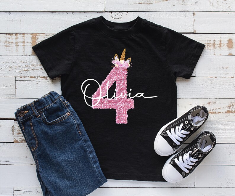 May include: Black t-shirt featuring a pink glittery number 4 unicorn design and the name "Olivia" in white script. The image includes blue denim jeans and black canvas trainers with white soles and laces.