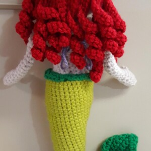 Peut inclure: Une poup&eacute;e sir&egrave;ne au crochet faite &agrave; la main avec des cheveux rouge vif, des bras blancs, une queue verte et jaune et une nageoire verte. La poup&eacute;e est faite avec du fil et a une apparence fantaisiste et artisanale. La sir&egrave;ne est un jouet doux unique.
