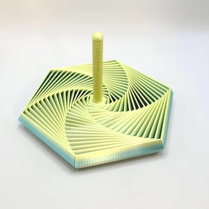 May include: A yellow and blue geometric design object with a central vertical post. The base is a hexagon with a spiral pattern. The post is cylindrical with a textured surface. The object is likely a decorative item or a stand.