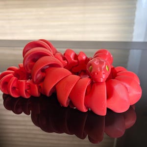 May include: A red plastic snake toy with a coiled body and a green head. The snake is made up of multiple connected segments.