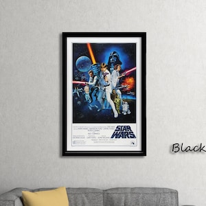 Op de afbeelding: Een ingelijste Star Wars-filmposter met een zwart frame. De poster toont personages uit de film, waaronder Darth Vader, Luke Skywalker en Princess Leia. De poster wordt in een woonkamer getoond.