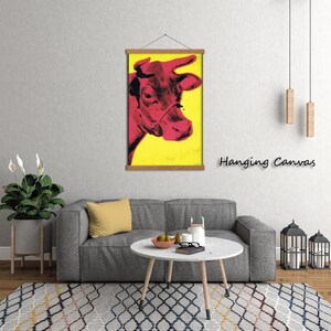 May include: A pop art style print of a cow's head in shades of red against a yellow background. The artwork is displayed on a wooden hanging frame. The words "Hanging Canvas" are printed in black on the right side of the image.