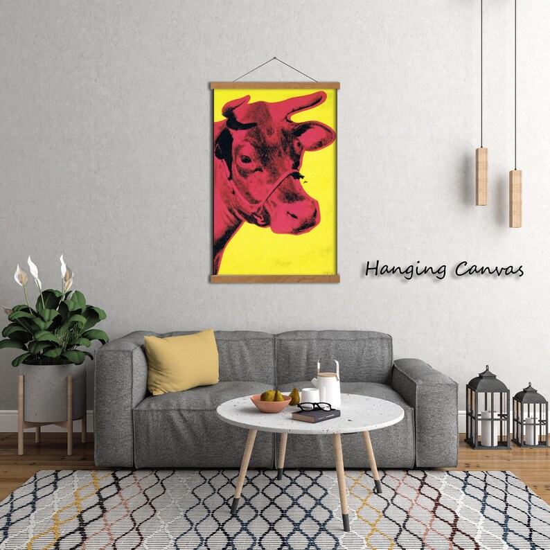 May include: A pop art style print of a cow's head in shades of red against a yellow background. The artwork is displayed on a wooden hanging frame. The words "Hanging Canvas" are printed in black on the right side of the image.
