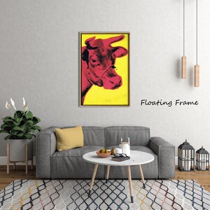 May include: A framed pop art print featuring a red cow against a yellow background. The cow's head is in profile, with the text "Floating Frame" in black. The artwork is displayed above a gray sofa in a living room setting.