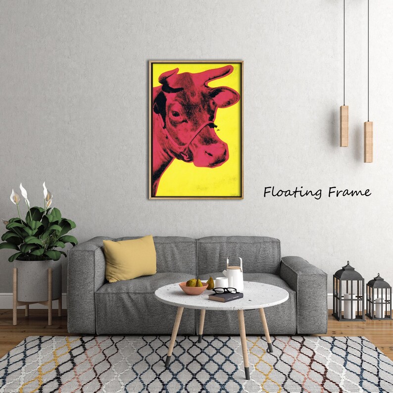 May include: A framed pop art print featuring a red cow against a yellow background. The cow's head is in profile, with the text "Floating Frame" in black. The artwork is displayed above a gray sofa in a living room setting.