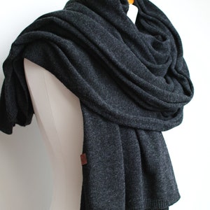 May include: A charcoal gray knitted scarf with a brown leather tag. The scarf is draped over a white mannequin.