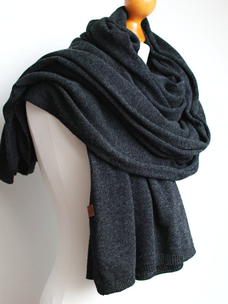 May include: A charcoal gray knitted scarf with a brown leather tag. The scarf is draped over a white mannequin.