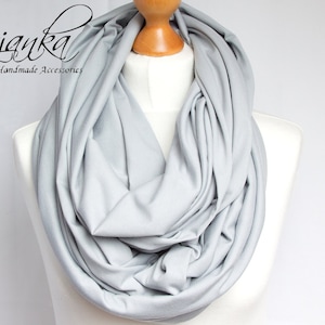 May include: A light gray infinity scarf made of soft fabric. The scarf is draped over a mannequin's neck.