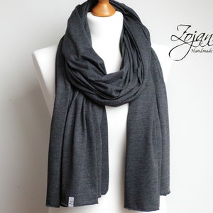 Puede incluir: Una bufanda gris antracita de tejido suave y elástico. La bufanda está drapeada sobre un maniquí blanco.