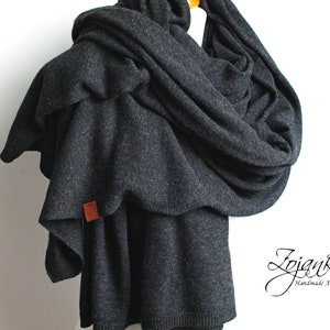 May include: A charcoal grey infinity scarf made of soft knit fabric. The scarf is draped over a mannequin and has a small brown leather tag attached.