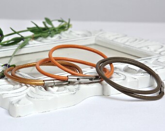 May include: Three leather bracelets in brown, orange, and gold tones. The bracelets are stacked on top of each other and have a silver clasp.
