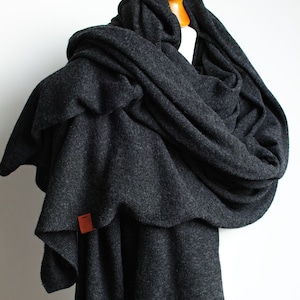 May include: A charcoal gray knitted scarf draped over a mannequin. The scarf is made of a soft, textured fabric and has a small brown leather tag.
