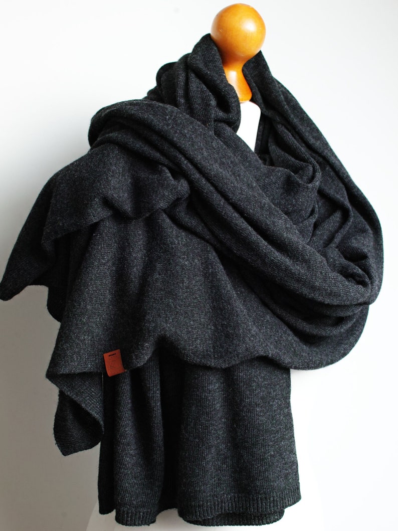 May include: A charcoal gray knitted scarf draped over a mannequin. The scarf is made of a soft, textured fabric and has a small brown leather tag.