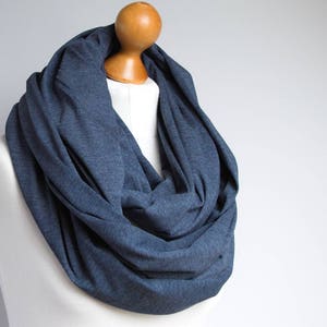 May include: A soft, blue infinity scarf made of a knitted fabric. The scarf is draped over a wooden mannequin.