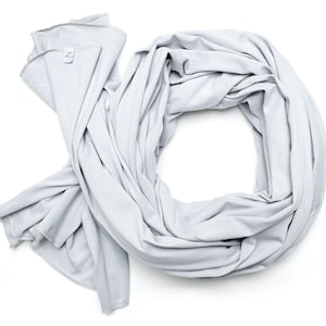 Può includere: Una sciarpa a cerchio grigio chiaro in tessuto morbido, drappeggiata a forma circolare. La sciarpa è su sfondo bianco. È visibile una piccola etichetta con la lettera "Z".