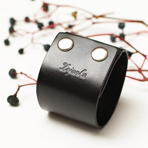 May include: Black leather cuff bracelet with silver snaps and the word "Izabela" embossed on the front.