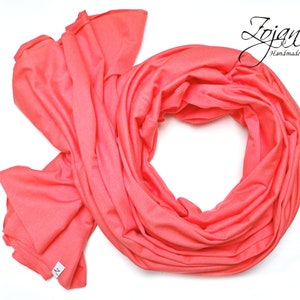 May include: A coral colored infinity scarf made of soft fabric. The scarf is folded and arranged in a circle shape.