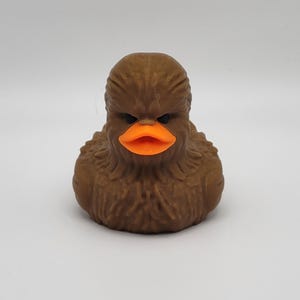 Peut inclure: Un canard en caoutchouc brun avec un design Chewbacca. Le canard a un grand bec orange et du fourrure brun.