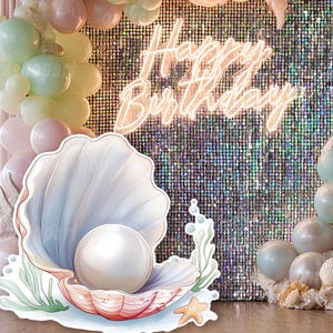 Könnte beinhalten: Eine digitale Requisite für eine Geburtstagsfeier, mit einer großen Muschel mit einer Perle, Luftballons und den Worten "Happy Birthday" in Neon. Der Hintergrund ist eine Paillettenwand mit rosa und grünen Luftballons.