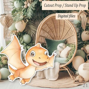May include: A cutout prop of a cartoon orange dinosaur with outstretched wings. The dinosaur is smiling. The background includes a wicker chair, pillows, and greenery. Text reads "Cutout Prop / Stand Up Prop" and "Digital files".