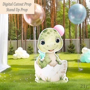 May include: A digital cutout prop of a baby dinosaur hatching from an egg, with a green and white color scheme. The prop is set on a grassy lawn with balloons in the background. Text on the image reads "Digital Cutout Prop Stand Up Prop."