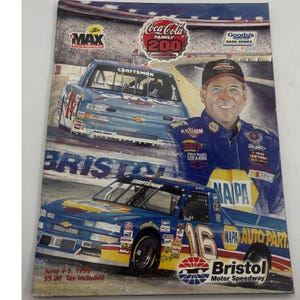 Könnte beinhalten: Ein Vintage-Rennprogramm-Cover mit einem Porträt eines Fahrers und zwei blauen Rennwagen. Die Autos zeigen Sponsorenlogos wie "Craftsman" und "NAPA". Das Cover enthält auch den Text "Coca-Cola Family 200" und "Bristol Motor Speedway."