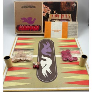 Puede incluir: Juego de Backgammon vintage con un tablero beige y rojo. La caja muestra el nombre del juego y un logotipo de pájaro. Incluye dados, fichas y un libro de reglas. El tablero de juego mide aproximadamente 51 cm por 38 cm.