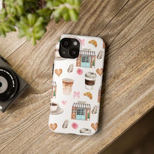 May include: White iPhone case with a watercolor pattern of coffee cups, croissants, hearts, and a coffee shop storefront. The text "Coffee Shop" is visible on the storefront.