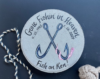 Peut inclure: Un mémorial rond en béton avec le texte "Gone Fishin' in Heaven" et les dates "11.22.1943" et "1.26.2021". Deux hameçons de pêche croisés sont peints sur le mémorial avec un ver rose sur un hameçon. Le texte "Fish on Ken!" est écrit sous les hameçons.