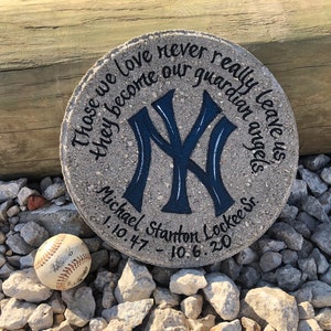 Puede incluir: Una piedra conmemorativa de hormig&oacute;n gris con un logotipo de los New York Yankees azul y blanco pintado en ella. La piedra tiene el texto "Those we love never really leave us they become our guardian angels" y "Michael Stanton Lockee Sr. 1.10.47 - 10.6.20" escrito en ella.