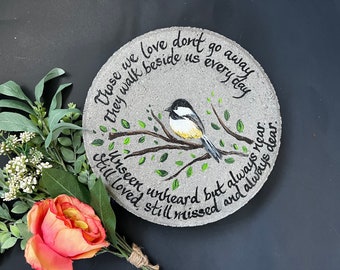 Puede incluir: Una piedra de jardín redonda de hormigón gris con un carbonero pintado a mano en blanco y negro sobre una rama marrón con hojas verdes. El texto dice: Those we love don't go away they walk beside us every day unseen unheard but always near still loved still missed and always dear.