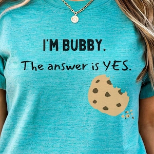 May include: A turquoise blue t-shirt with the text "I'm Bubby. The answer is YES." and a brown cookie with a bite taken out of it.
