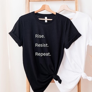 May include: Black t-shirt with the text "Rise. Resist. Repeat." printed in white.