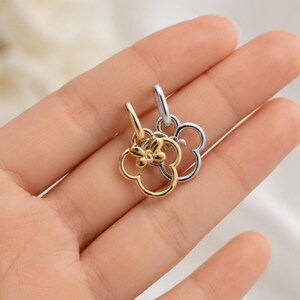 Puede incluir: Dos dijes de metal, uno de tono dorado y otro de tono plateado, cada uno con forma de flor de cuatro p&eacute;talos con un peque&ntilde;o detalle de lazo en la parte superior. Cada dije cuenta con una anilla circular en la parte superior para su fijaci&oacute;n.