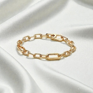 May include: A gold-colored chain link bracelet with a lobster clasp. The bracelet is made of a series of oval and rectangular links. The jewelry is displayed on a white, silky surface.