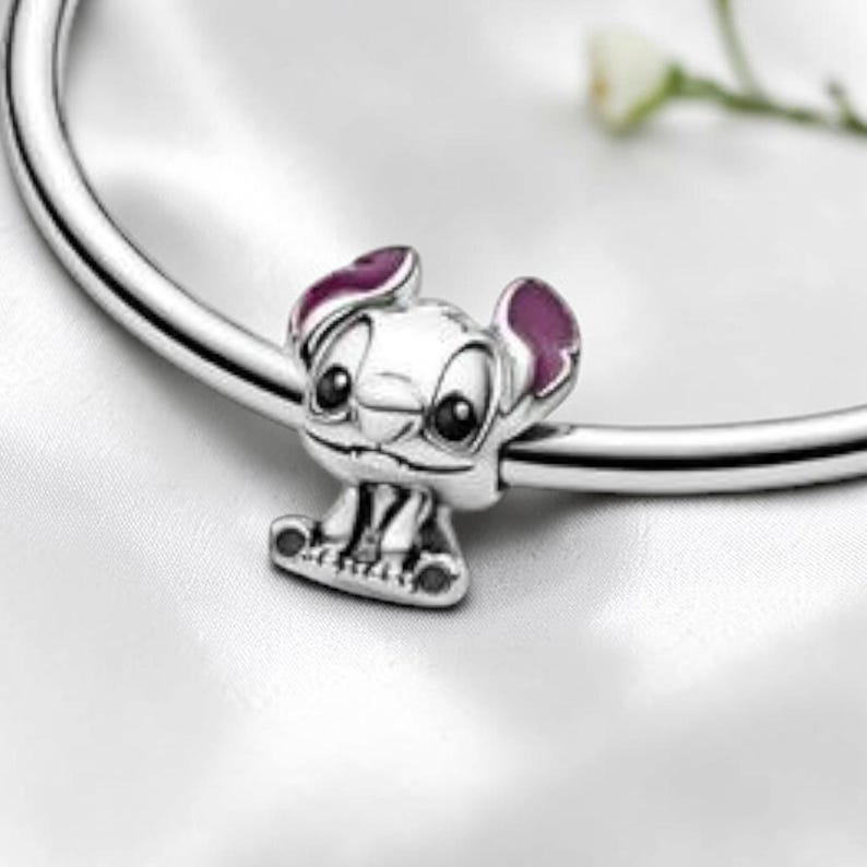 May include: A silver charm bead shaped like the character Stitch, featuring large black eyes and purple enamel accents on the inner ears, threaded onto a polished silver bracelet band. The charm displays a detailed facial expression.