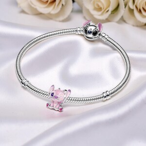 Peut inclure: Un bracelet &agrave; breloques en argent avec un charm de personnage de dessin anim&eacute; et un fermoir en forme de personnage. Les breloques sont roses et argent&eacute;es, sur un fond de satin blanc. Le bracelet est de style cha&icirc;ne serpent.