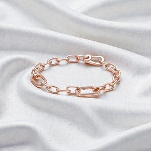 May include: Rose gold chain link bracelet with a lobster clasp. The bracelet features interconnected oval and rectangular links. The jewellery is displayed on white, silky fabric.