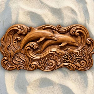 May include: A rectangular wooden wall carving featuring two dolphins swimming through stylized waves. The relief sculpture includes detailed depictions of coral, seaweed, and a spiral seashell at the bottom, all rendered in a warm, polished brown wood tone.
