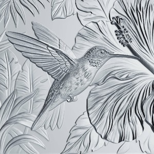 May include: A monochromatic silver-toned relief panel featuring a detailed hummingbird in flight, positioned near a large hibiscus flower. The design includes textured tropical foliage and leaves surrounding the central bird and flower motif.