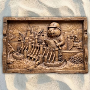 May include: A carved wooden relief showing a beaver in a hard hat studying blueprints for a dam and castle. The artwork has detailed elements of the dam's structure, cranes, and landscape, with other beavers in the background.