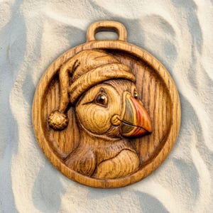 May include: A circular wooden wall hanging featuring a relief carving of a puffin wearing a knit cap. The puffin has a multi-colored beak with orange, yellow, and black tones. The wood grain is visible throughout the natural brown finish.