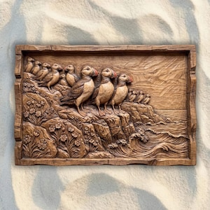 May include: A rectangular wooden wall plaque featuring a detailed relief carving of a group of puffins standing on a rocky cliffside overlooking the ocean. The scene includes carved flowers in the foreground and waves crashing against the base.